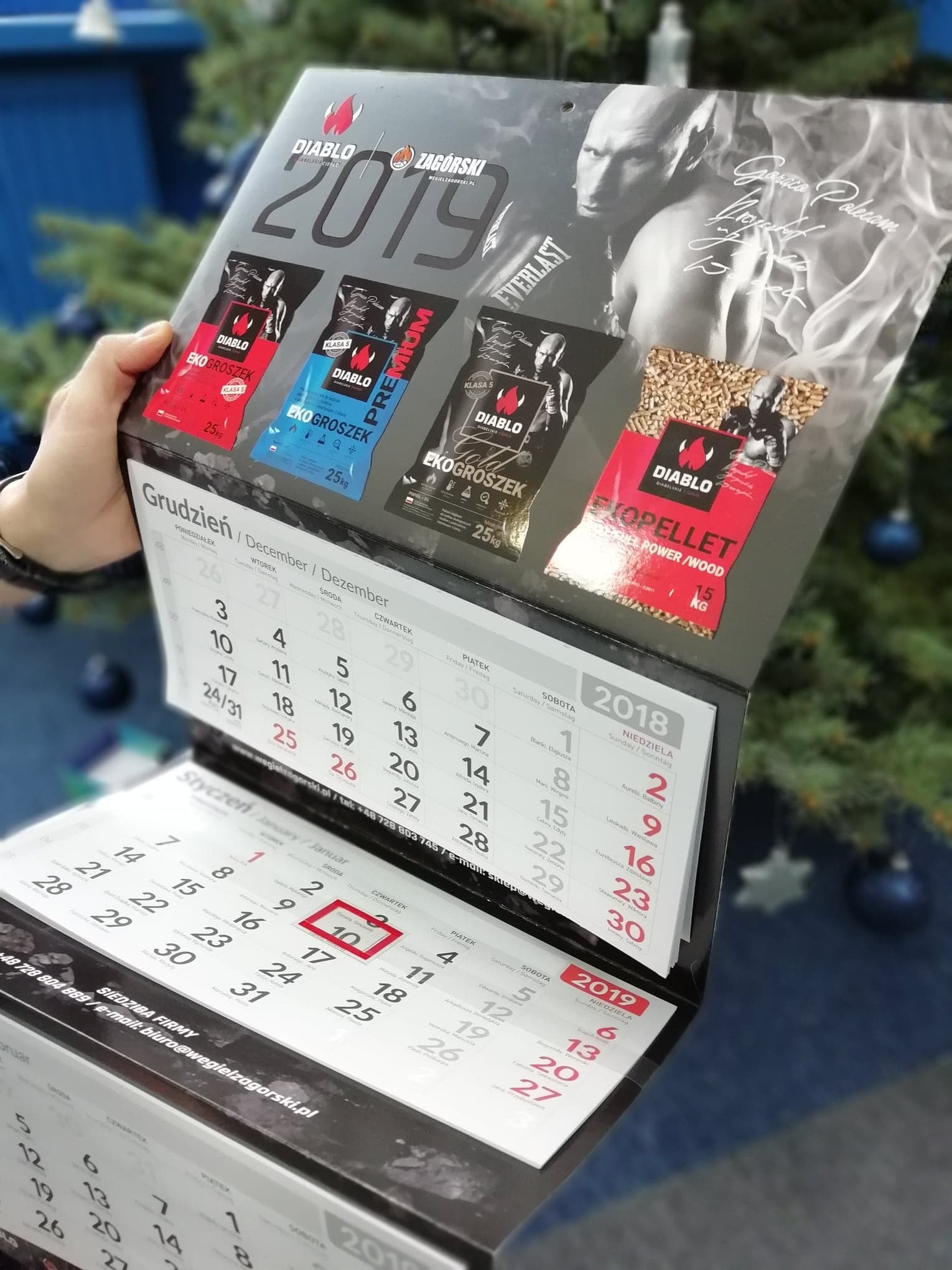 Kalendarz firmowy 2019 z wizerunkiem boksera i workami ekogroszku oraz pelletu na tle choinki.