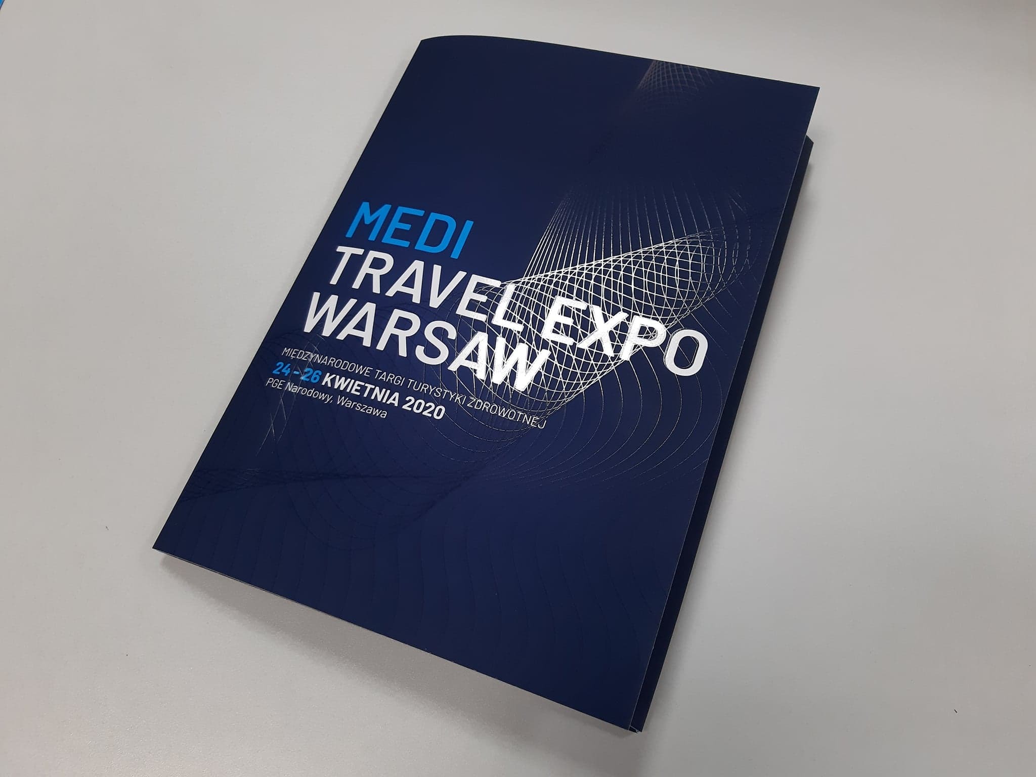 Broszura informacyjna targów turystyki zdrowotnej Medi Travel Expo Warsaw 2020, z datą 24-26 kwietnia i miejscem PGE Narodowy w Warszawie, na ciemnoniebieskim tle z srebrnymi elementami graficznymi.