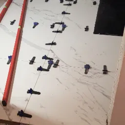 Układanie białych i czarnych marmurkowych płytek z użyciem klips&oacute;w poziomujących i poziomicy, widoczny surowy beton na podłodze.