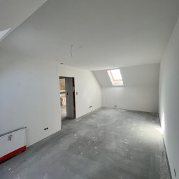 BenBud - Poddasze po świeżym malowaniu na biało, widoczne ślady po pracach na szarym betonie, okno dachowe wpuszczające jasne światło, przygotowane do dalszych prac wykończeniowych.