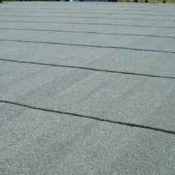 Szary, płaski dach pokryty papą z widocznymi zgrzewami, wykonany w słoneczny dzień.