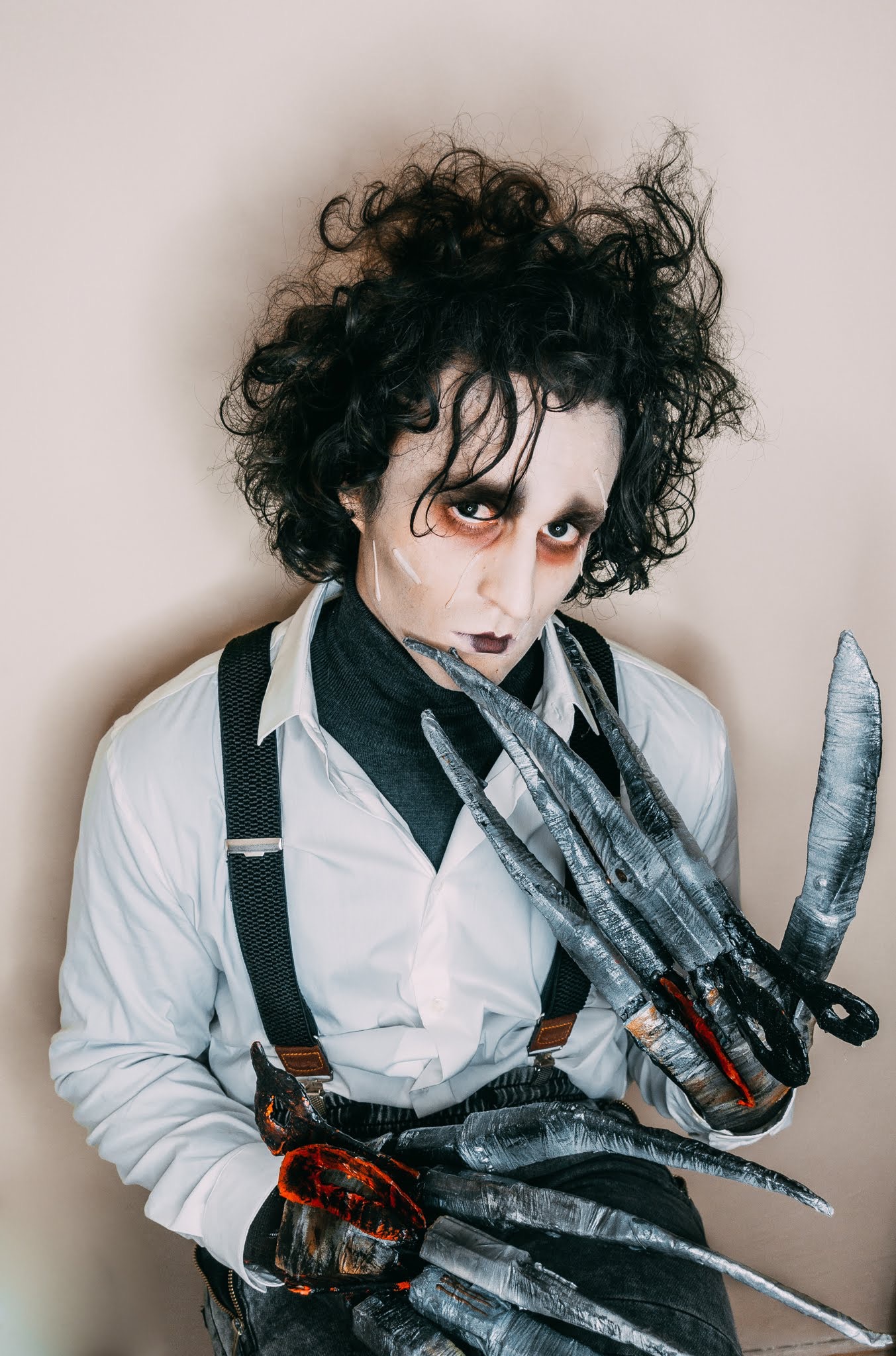 Osoba w charakteryzacji Edwarda Nożycorękiego z bladą cerą, ciemnymi ustami, podkreślonymi oczami i nożycami zamiast dłoni, ubrana w białą koszulę i szelki