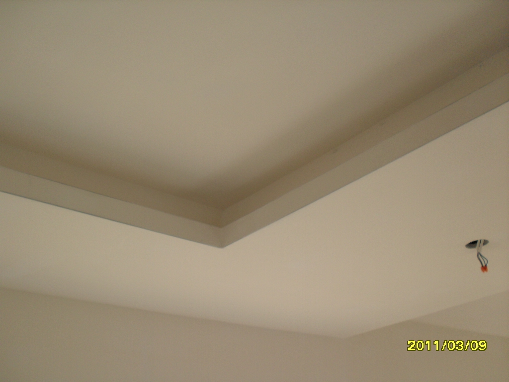 Wykończony sufit podwieszany z widocznym otworem na oświetlenie i wystającymi przewodami, sfotografowany pod kątem.