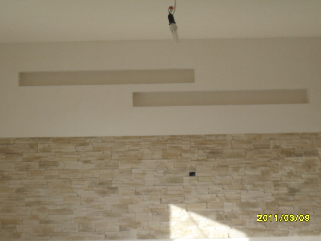 Ściana wykończona kamieniem dekoracyjnym, z dwoma wnękami w górnej części ściany oraz widoczną żarówką na suficie.