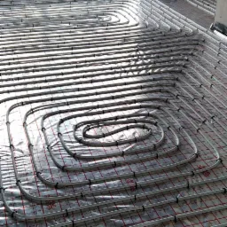 Rozłożone rury ogrzewania podłogowego na folii z siatką, widok z góry, w tle okno i surowe ściany