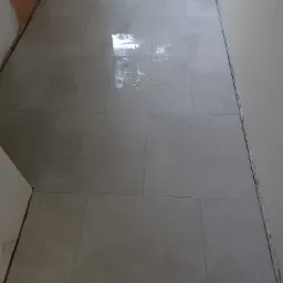 Świeżo ułożone, duże, prostokątne płytki podłogowe w odcieniach szarości, z widocznymi fugami, w trakcie prac wykończeniowych, z surowymi krawędziami ścian.