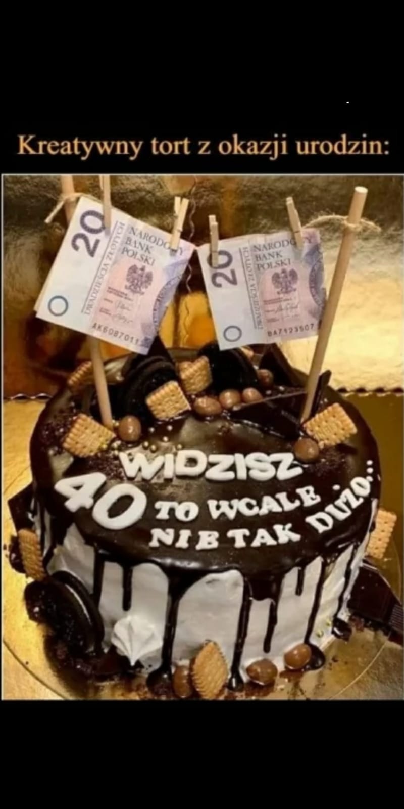 Tort urodzinowy z polewą czekoladową, dekorowany biszkoptami, orzechami i dwoma banknotami 20 zł przymocowanymi do patyczków jak chorągiewki, z napisem '40 Widzisz to wcale nie tak dużo'.