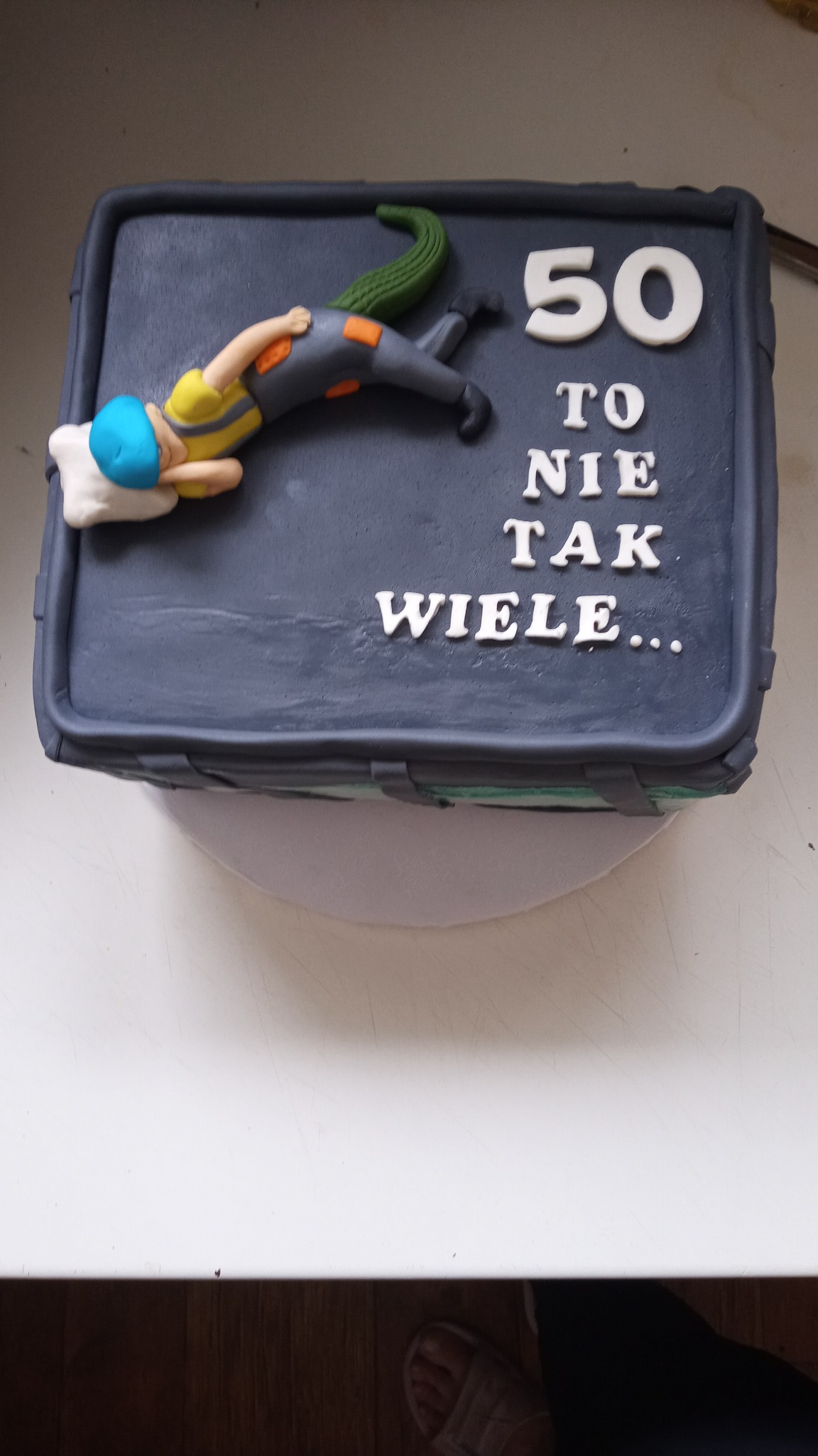Tort urodzinowy w kształcie walizki z figurką śpiącego nurka i napisem '50 to nie tak wiele...'
