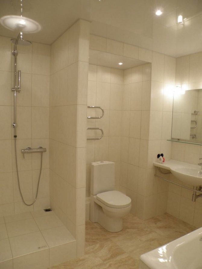 Jasna łazienka po remoncie z kabiną prysznicową, toaletą i umywalką, wykończona płytkami w odcieniach beżu, z dekoracyjną figurką na półce.