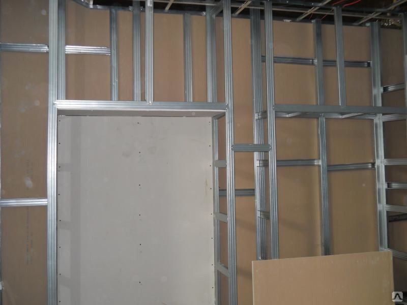 Konstrukcja szkieletowa z profili metalowych, przygotowana pod montaż okładzin ściennych, widoczne płyty OSB i fragment niezamontowanej płyty na pierwszym planie.