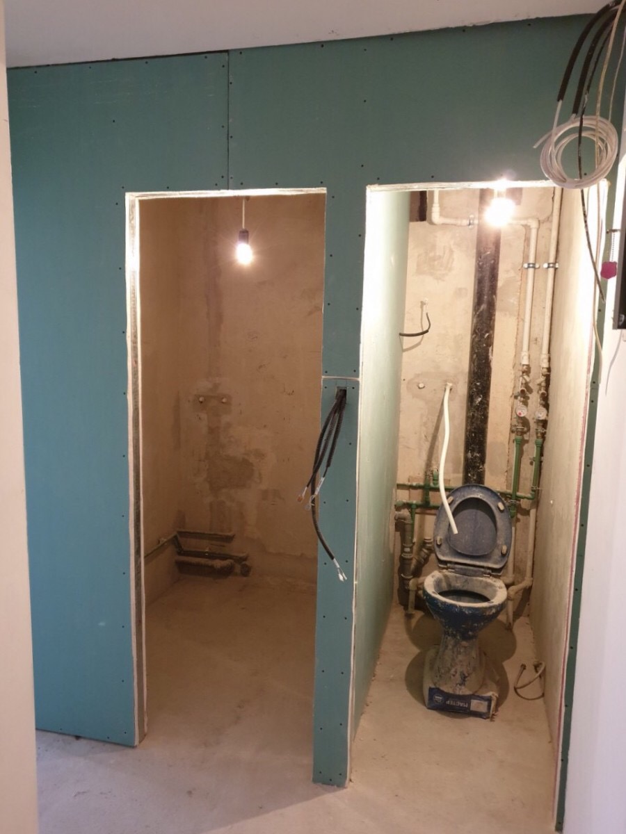 Wnętrze łazienki w trakcie prac remontowych z widoczną instalacją hydrauliczną i toaletą w osłonie z płyt kartonowo-gipsowych, surowy stan wykończenia.