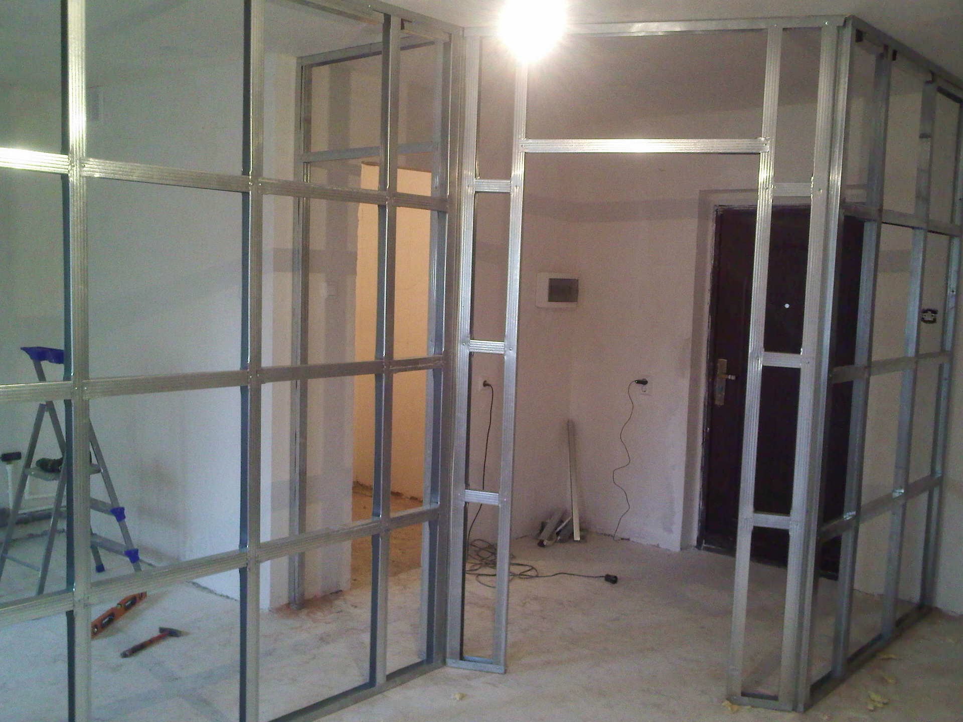 Konstrukcja ścianki działowej ze stalowych profili, widoczna drabina aluminiowa i narzędzia na podłodze w trakcie montażu.