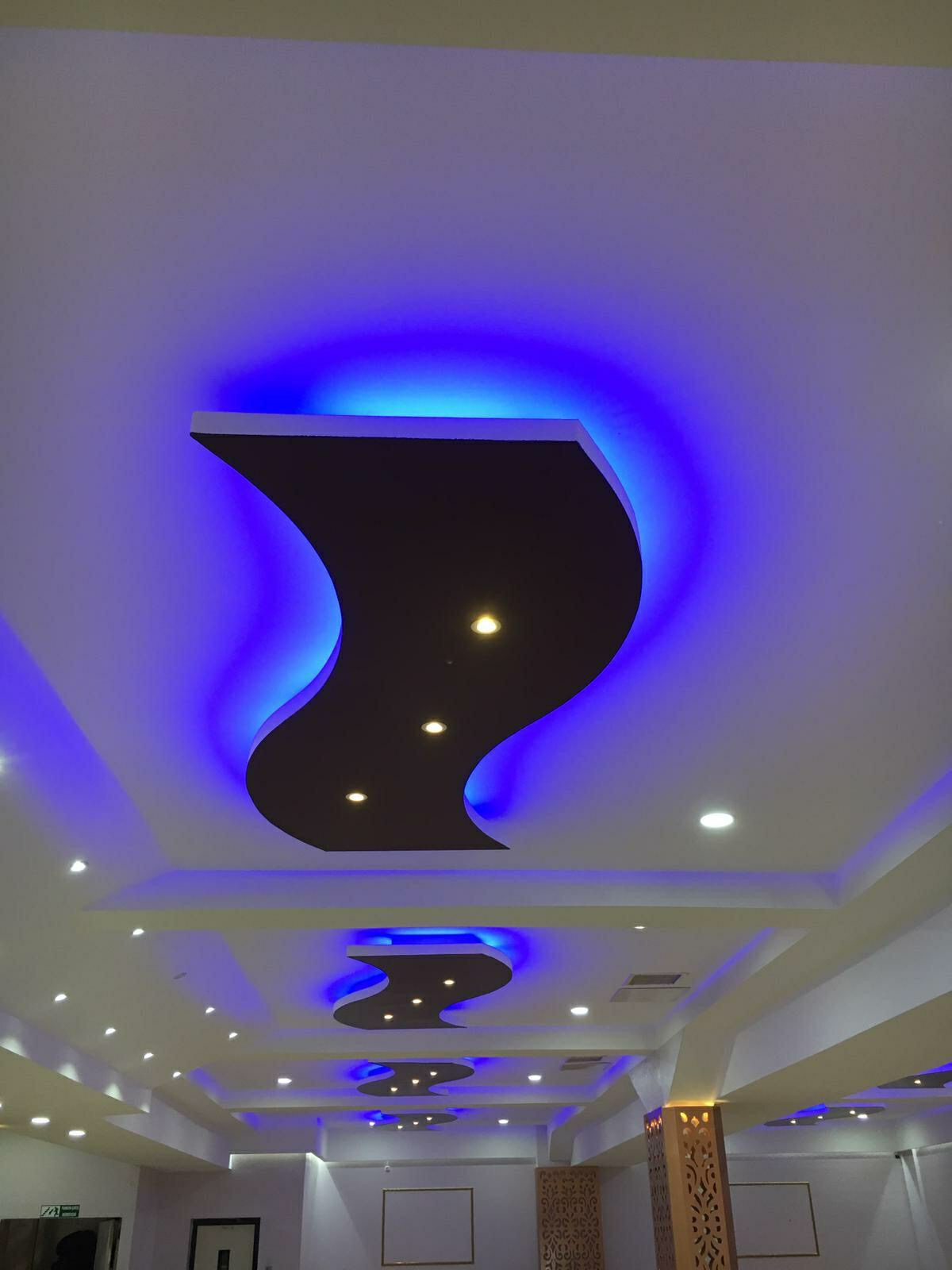 Sufit podwieszany z płyty karton gips z oświetleniem LED w kolorze niebieskim i punktowymi lampami halogenowymi, widoczne elementy dekoracyjne na kolumnach.