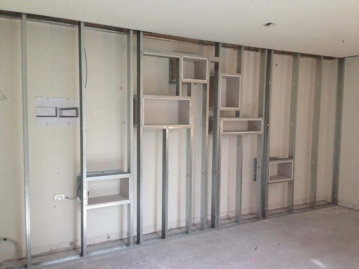 Stelaż z profili stalowych do zabudowy ściany z płyt kartonowo-gipsowych z wnękami na półki, widoczne przewody elektryczne i puszka instalacyjna.