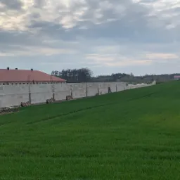 Budowa budynku gospodarczego z bloczków betonu komórkowego na tle zielonego pola i pochmurnego nieba.