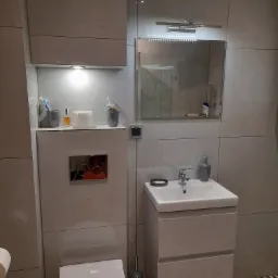 Jasna łazienka w Bytomiu z podwieszaną toaletą, umywalką z szafką i dużym lustrem z oświetleniem LED, wykończona płytkami w odcieniach szarości i wzorzystą podłogą.