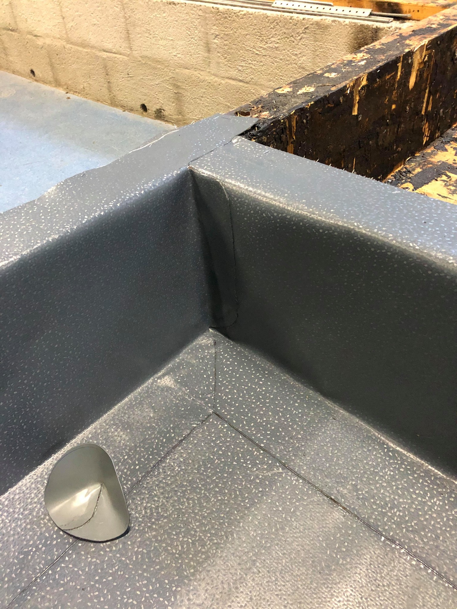 Szary, wzorzysty narożnik dachu z blachy z odpływem, widoczne łączenia blach na tle fragmentu konstrukcji drewnianej.