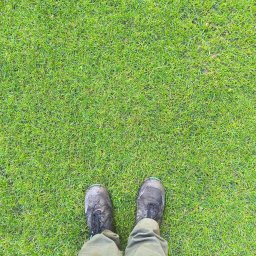 KADOKA Krzysztof Kamiński - Widok z góry na parę zabrudzonych butów trekkingowych stojących na gęstej, zielonej trawie.