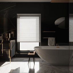 Magdalena Olejniczak Projektowanie Wnętrz - Elegancka, czarno-biała łazienka z marmurową posadzką, wolnostojącą wanną, czarną szafką z złotymi akcentami i oknem z żaluzjami, oświetlona promieniami słonecznymi padającymi przez okno.