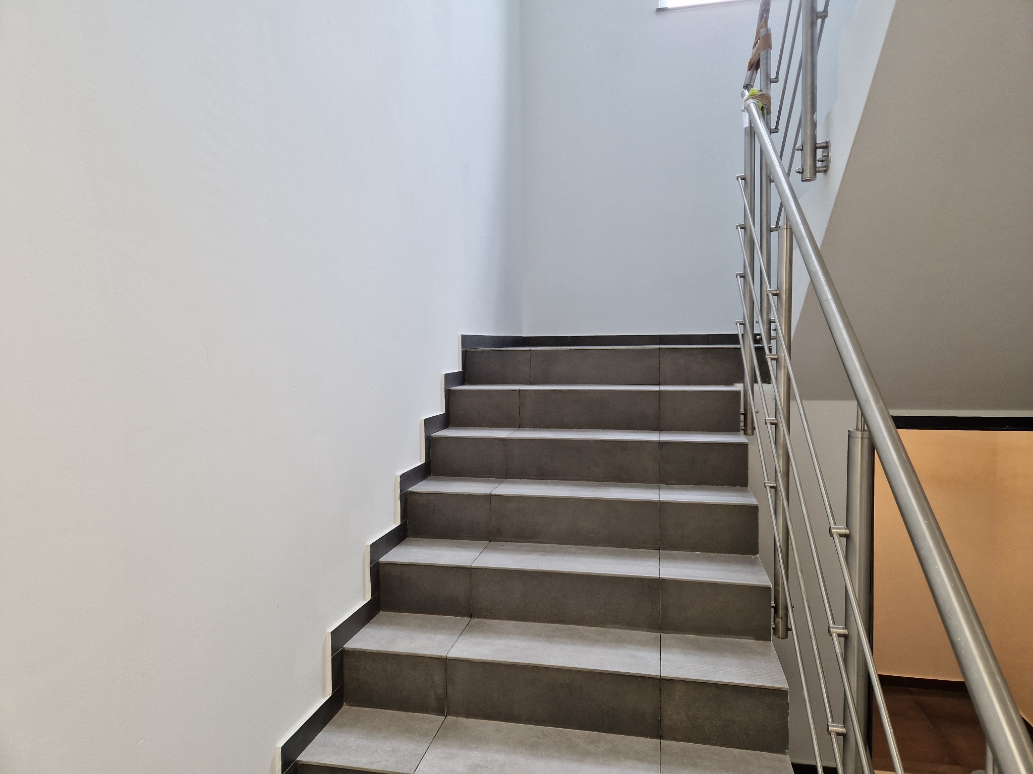 Schody wyłożone szarymi płytkami w budynku w Markach, z metalową balustradą i pomalowaną na biało ścianą.