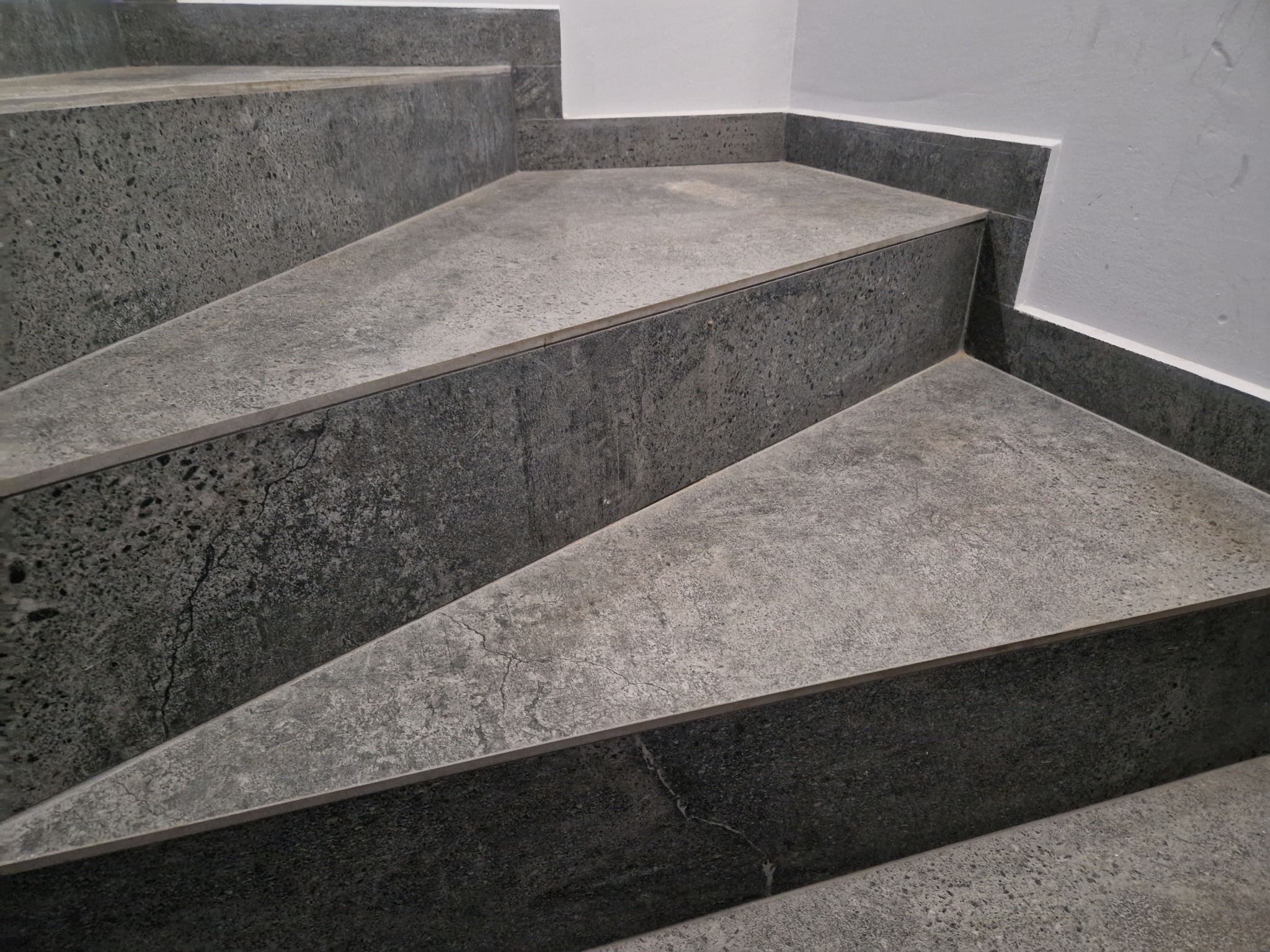 Schody wykończone szarym gresem, widoczne detale struktury płytek i fugi przy ścianie.