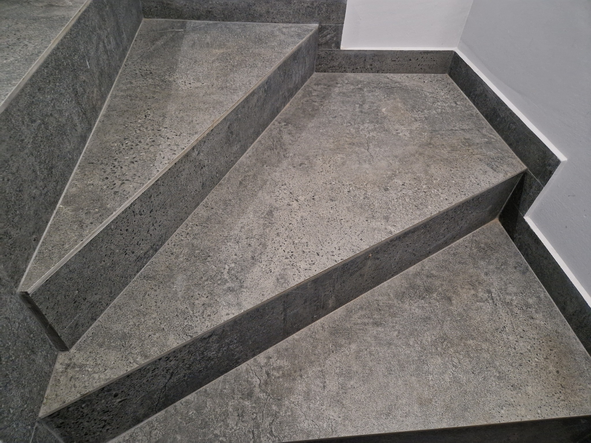 Schody wykończone szarą, nakrapianą płytką ceramiczną, widok z góry ukazuje precyzyjne ułożenie płytek i estetyczne wykończenie narożników.