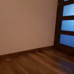 Ściana pomalowana na różowo, drewniana podłoga i ciemne drzwi z mlecznym szkłem w Bojanowie.