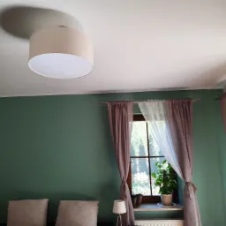 Pokój z zielonymi ścianami, beżowym abażurem lampy sufitowej, oknem z brązowymi i białymi zasłonami, rośliną w doniczce na parapecie i łóżkiem z beżowymi poduszkami.