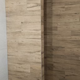 AMBITION Jarosław Rozwadowski - Wykończona łazienka z okładziną ścienną imitującą drewno, z widocznym fragmentem instalacji elektrycznej na suficie. Minimalistyczny design, ciepła kolorystyka.