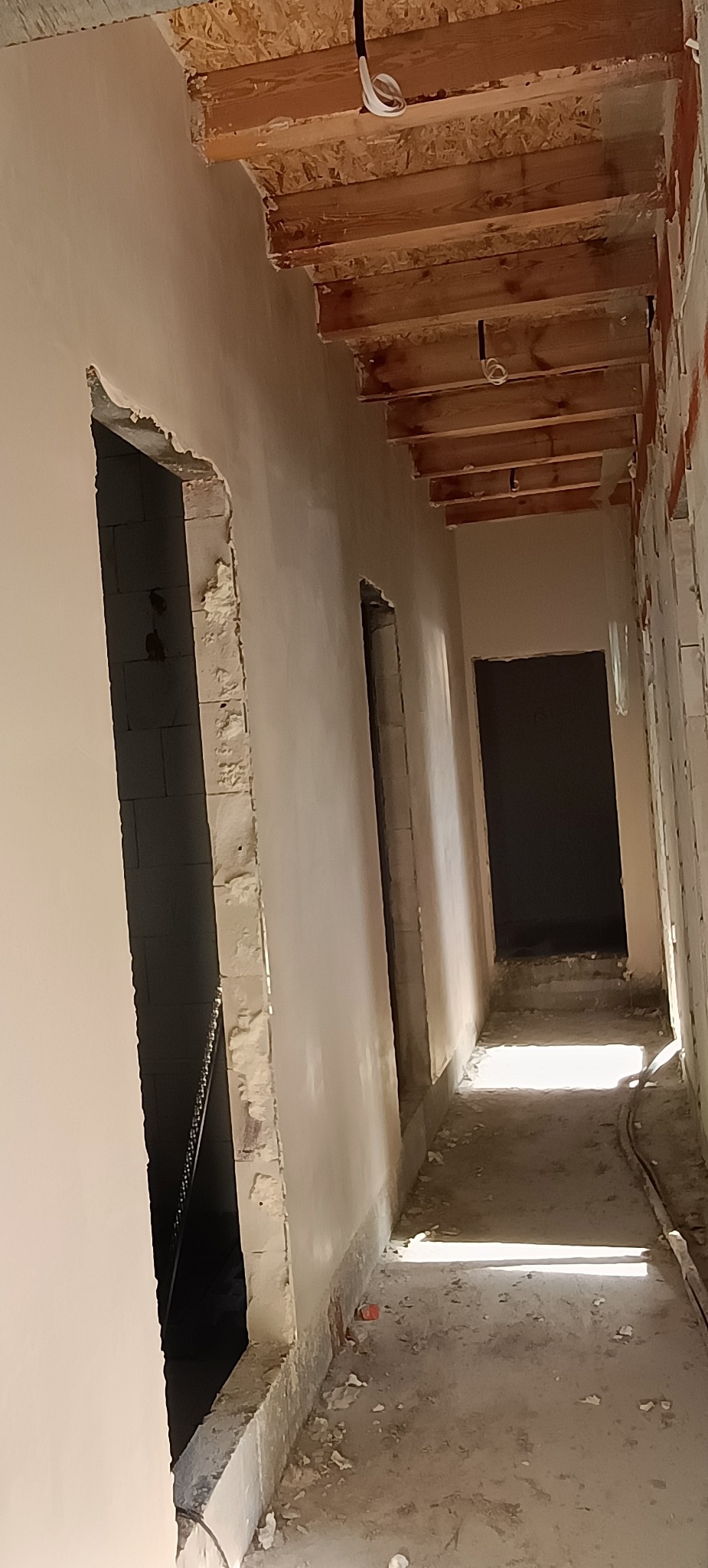 Wnętrze w trakcie prac tynkarskich: ściany pokryte świeżym tynkiem, widoczne surowe drewniane elementy stropu i otwory drzwiowe w stanie surowym. Tynk DOLINA NIDY ZETA.