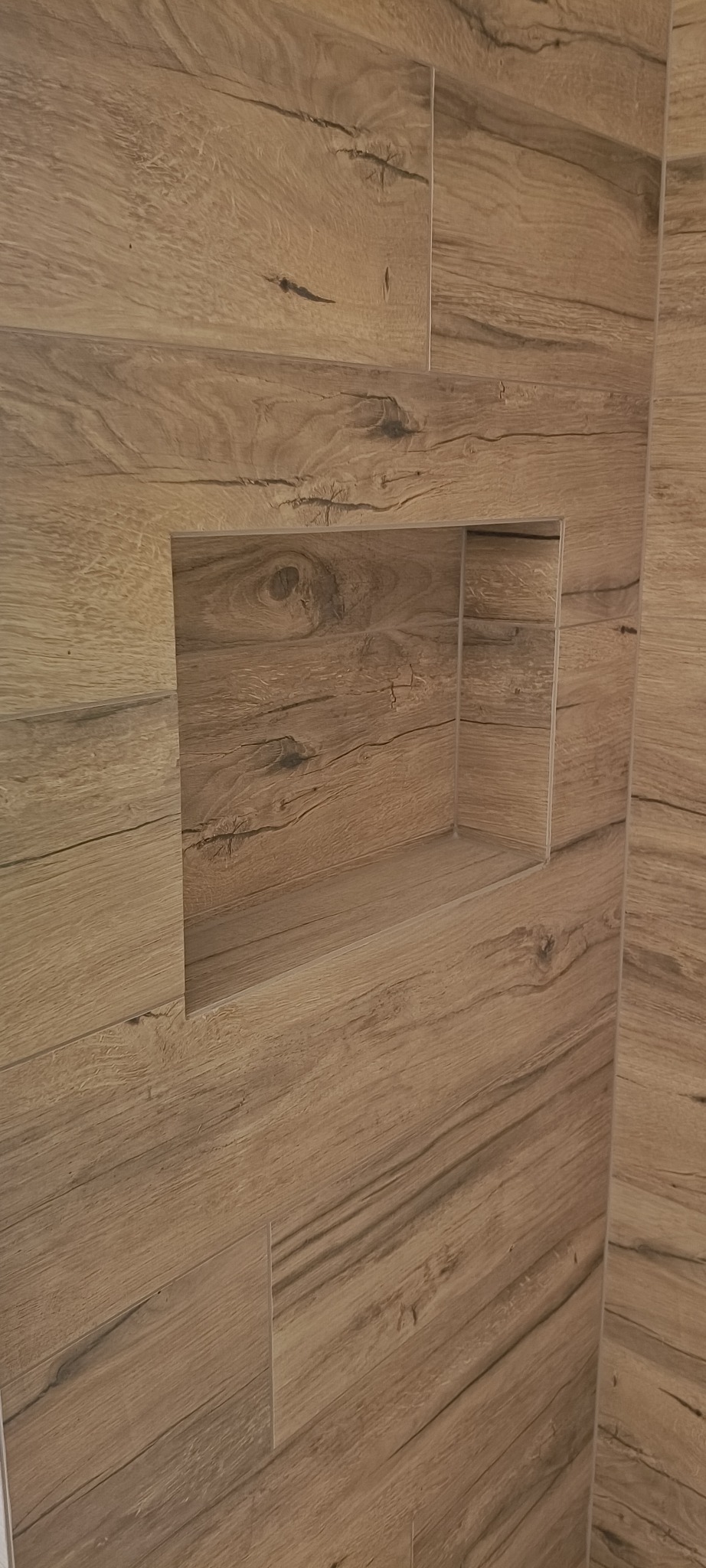 Ściana wyłożona płytkami imitującymi drewno z wnęką, ukazująca precyzję wykonania i estetyczne wykończenie. Detal wnęki podkreśla unikalny charakter aranżacji.