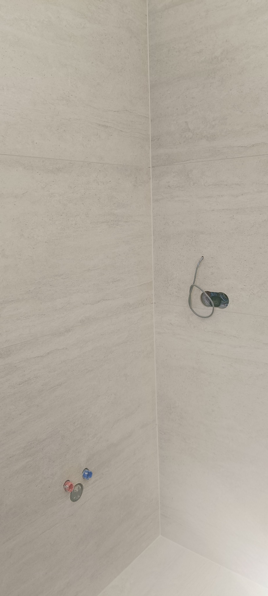 Wykończona łazienka z jasnymi, marmurkowymi płytkami. Widoczne przyłącza wodne i wyprowadzona instalacja elektryczna. Minimalistyczny design, świeżo po remoncie.