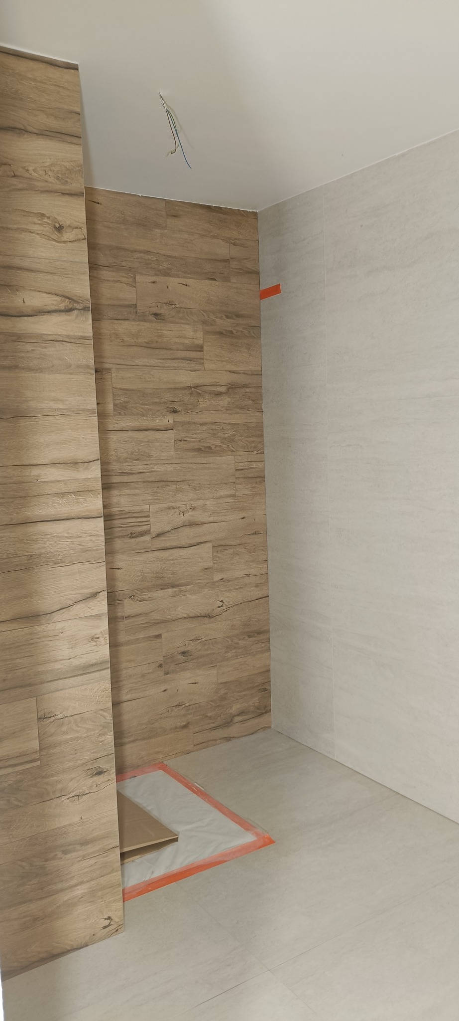 Wykończona łazienka z płytkami imitującymi drewno na ścianie i jasnymi płytkami na podłodze i drugiej ścianie. Widoczne wystające kable.