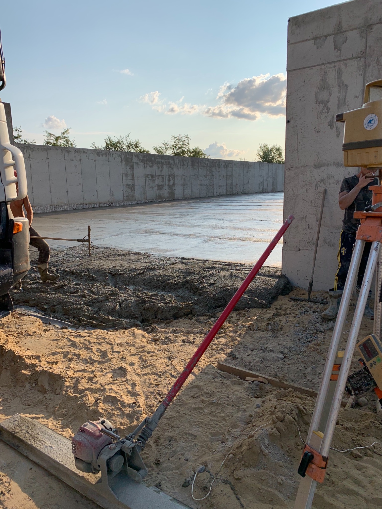 Wylewka betonowa na placu budowy w Fajsławicach, widoczny pracownik z łatą w tle, poziomica i ubijarka w piasku na pierwszym planie.