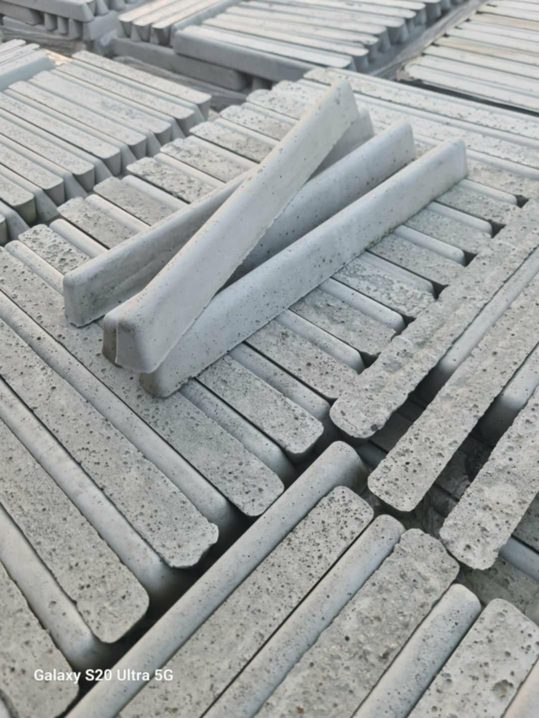 Szare, podłużne prefabrykaty betonowe ułożone równolegle, z widoczną porowatą strukturą betonu. Kilka elementów ułożonych na wierzchu pod kątem.