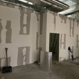 M-Bud - Wnętrze w trakcie prac wykończeniowych: ściany z płyt gipsowo-kartonowych z widocznymi łączeniami szpachlowymi w kształcie litery H, szpachelka, szlifierka do gipsu, drabina w przejściu, rury...