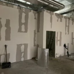 Wnętrze w trakcie prac wykończeniowych: ściany z płyt gipsowo-kartonowych z widocznymi łączeniami szpachlowymi w kształcie litery H, szpachelka, szlifierka do gipsu, drabina w przejściu, rury...