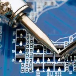 Lutownica precyzyjnie aplikująca cynę na element elektroniczny na niebieskiej płycie głównej, widoczne ślady topnika.