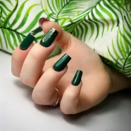 Kraków: Dłoń z ciemnozielonymi, kwadratowymi paznokciami, jeden z nich ozdobiony złotą folią, na tle tkaniny w tropikalne liście.