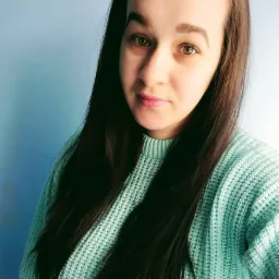 Portret młodej kobiety z długimi, ciemnymi włosami i zielonymi oczami, ubrana w miętowy sweter na tle jasnoniebieskiej ściany.