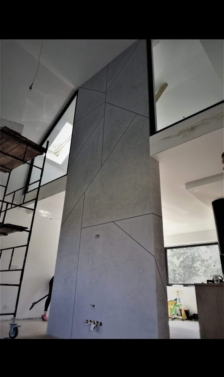 Wysoka ściana z dekoracyjnym wykończeniem w geometryczne wzory w Bydgoszczy, widoczny fragment rusztowania i instalacja wodna w dolnej części ściany.