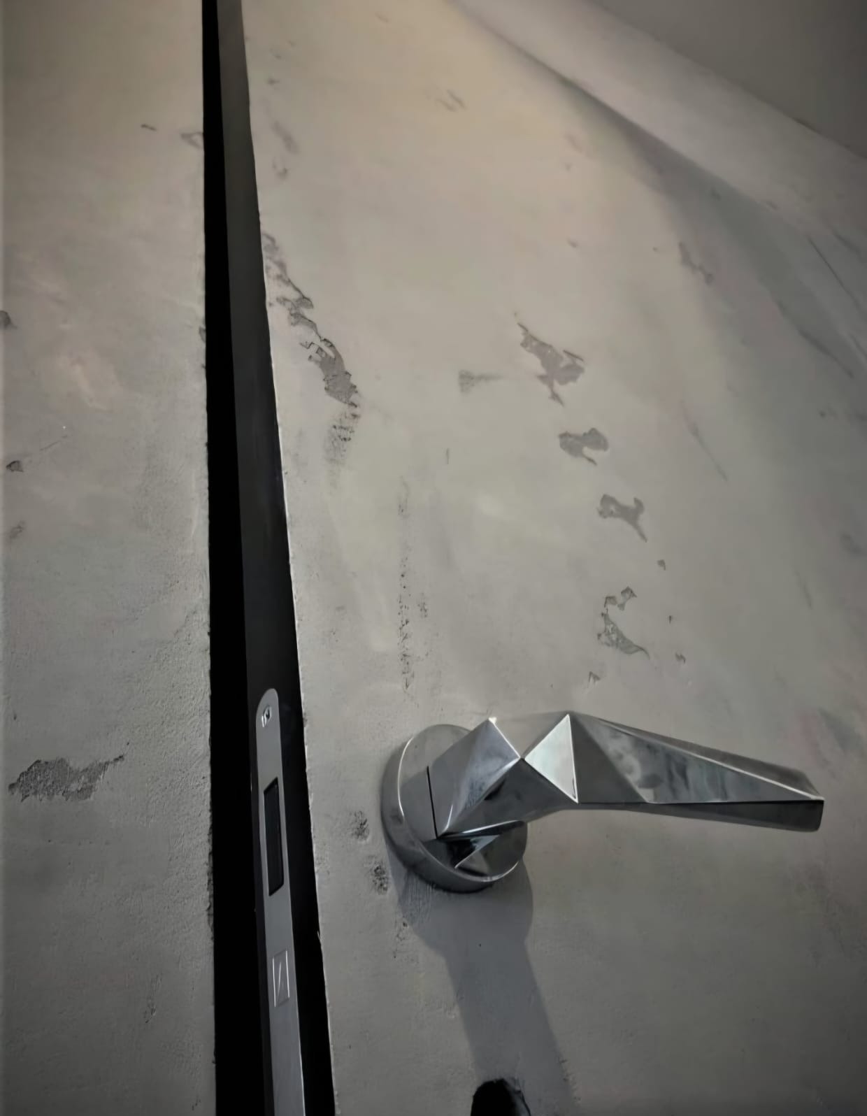 Szara ściana z efektem betonu i nowoczesna, geometryczna klamka. Widoczna czarna szczelina dylatacyjna. Minimalistyczny design wnętrza.