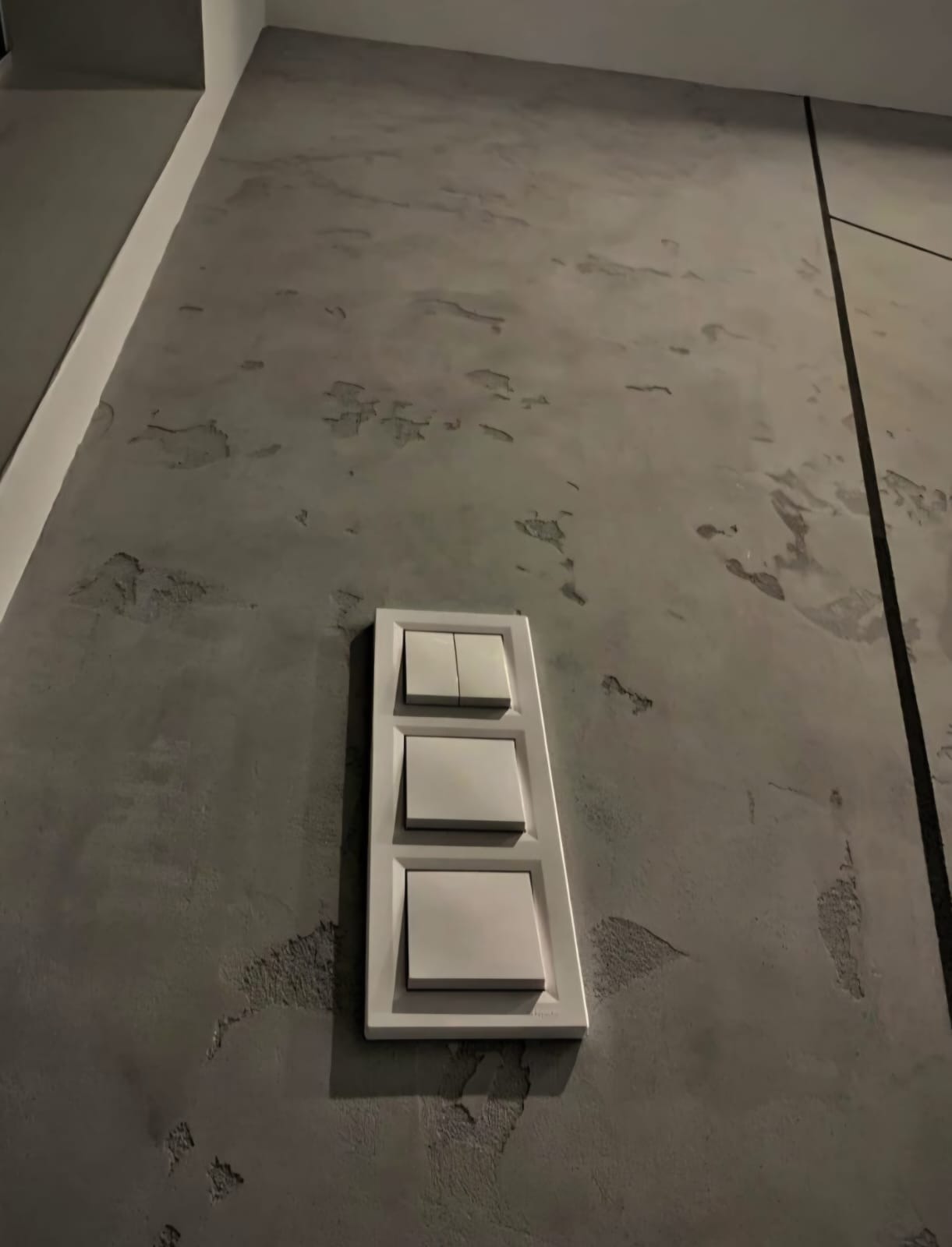 Szara ściana z dekoracyjnym tynkiem i potrójnym, białym włącznikiem światła. Minimalistyczne wykończenie wnętrza z bliska, z widoczną fakturą ściany.