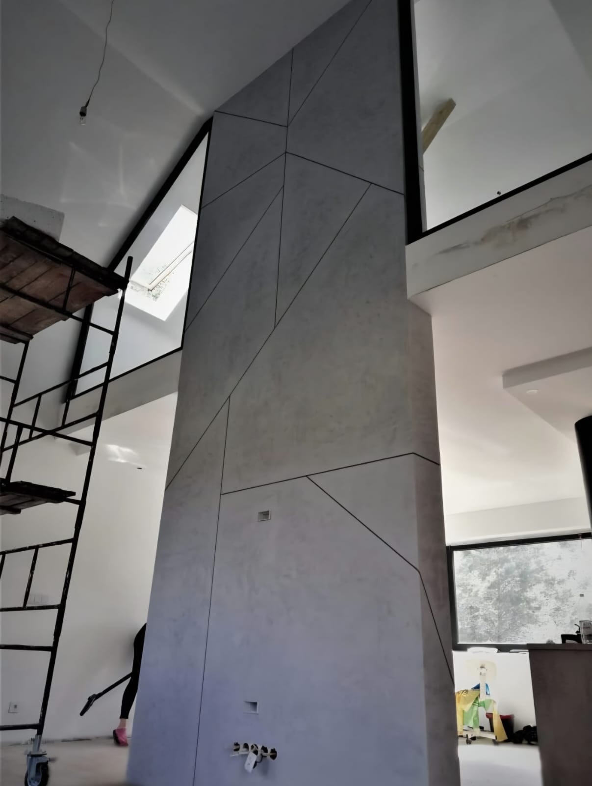 Wykończona ściana z dekoracyjnym tynkiem w geometryczne wzory, widoczne fragmenty rusztowania i okna, nowoczesne wnętrze w trakcie wykańczania.