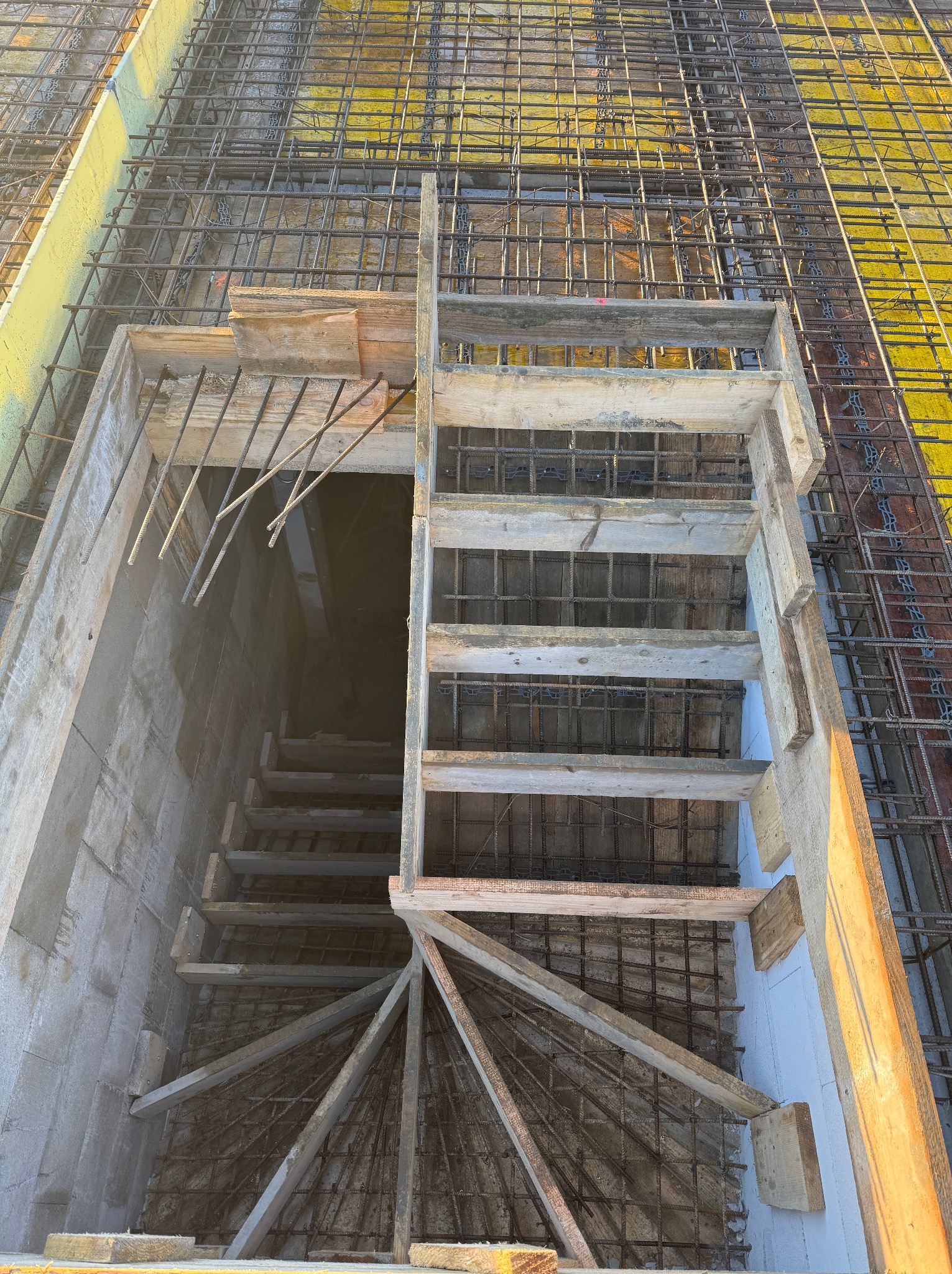 Zbrojenie fundamentów pod schody w Limanowej. Widok z góry na szalunek i siatkę zbrojeniową, przygotowane do zalania betonem. Drewniane schody tymczasowe.