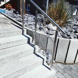 Fphu-Sam - Zewnętrzne schody z jasnego granitu z prostą, nowoczesną balustradą ze stali nierdzewnej i linkami, otoczone kamieniami i niskim murkiem z szarego granitu, z widocznym fragmentem elewacji budynku...