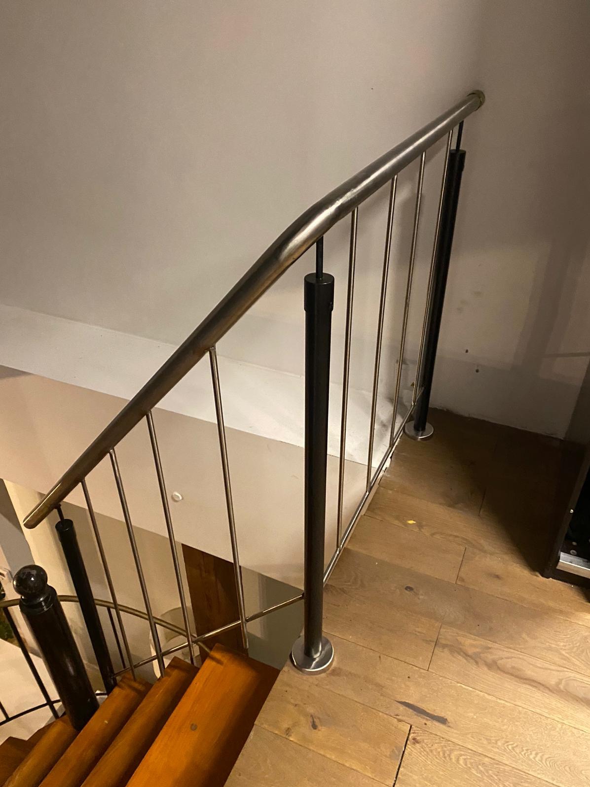 Wewnętrzne schody drewniane z metalową balustradą o pionowych szczeblach i czarnych słupkach, widok z góry na zakręt schodów.