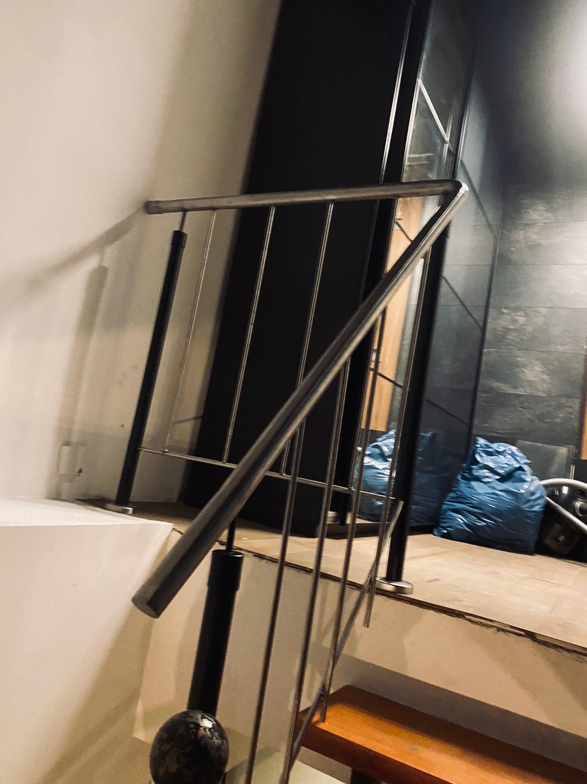 Metalowa balustrada schodowa z poprzecznymi prętami, widoczna z dołu, z workami budowlanymi w tle.