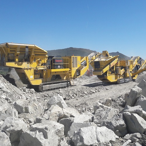 Żółty mobilny kruszarka do kamienia Keestrack na placu budowy z niebieskim niebem w tle.