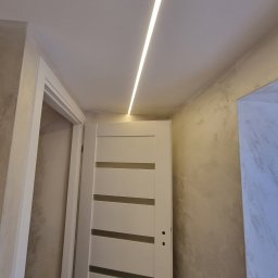 MIAREM - Zamknięte, białe drzwi wewnętrzne z poziomymi przeszkleniami, oświetlenie LED w suficie, ściany wykończone w stylu dekoracyjnym w Rawa Mazowiecka.